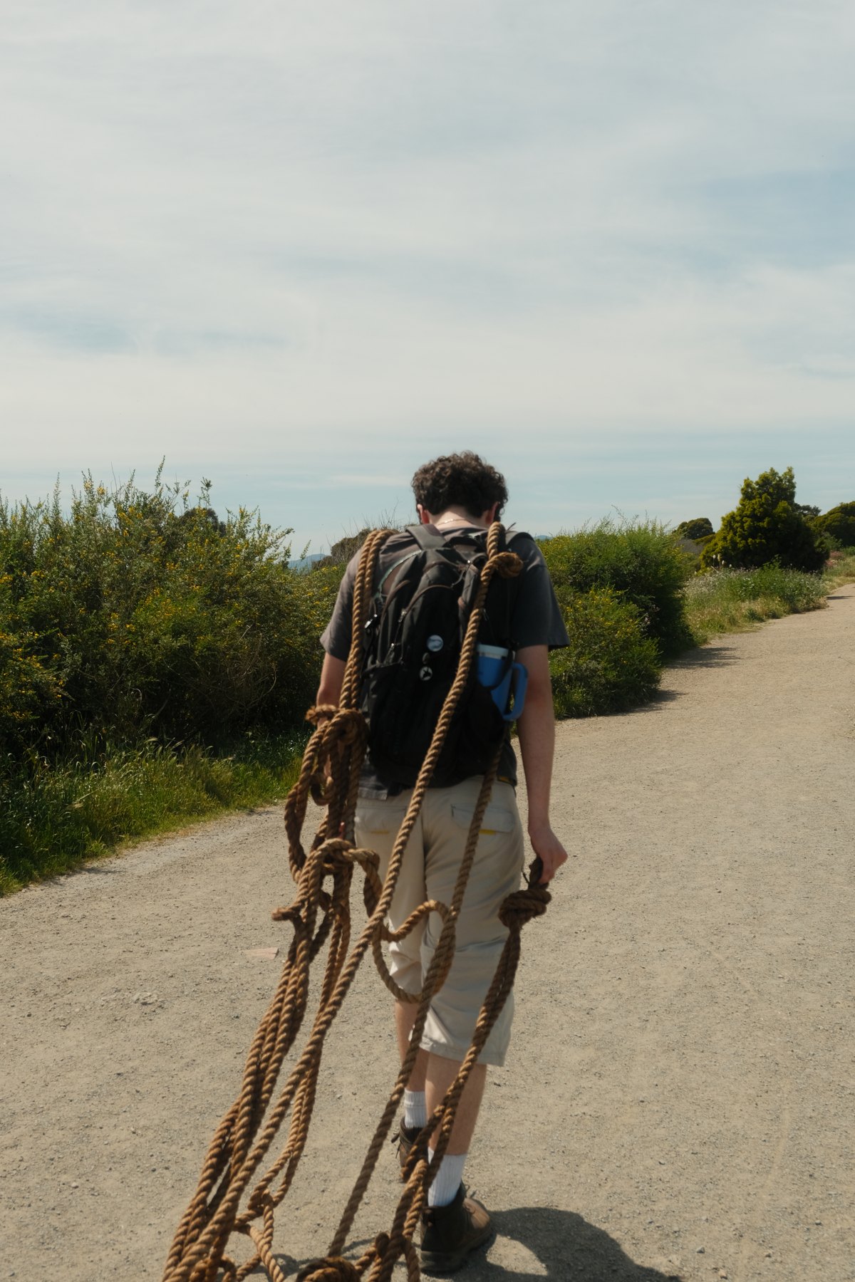 A model walking along a waterfront path carrying a bundle of rope.