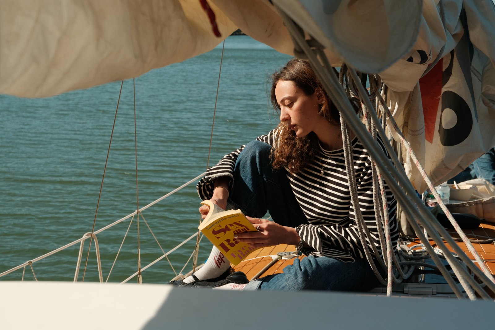 A model wearing a striped top beneath the sail, with ropes framing the scene.